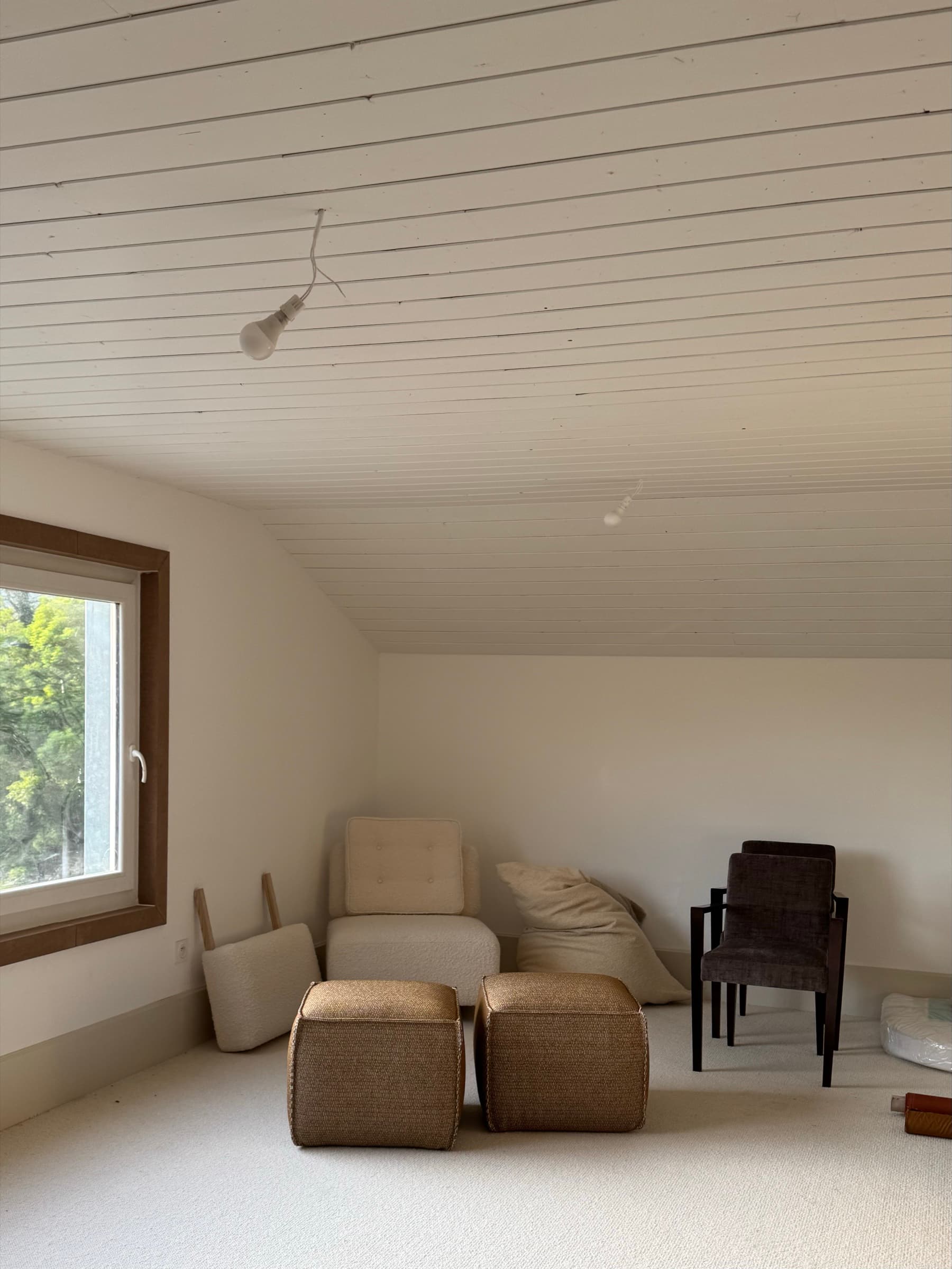 Espace showroom sous charpente en lambris blanc à Fleurie, fauteuil en bouclette crème, poufs tressés et sièges tapissés