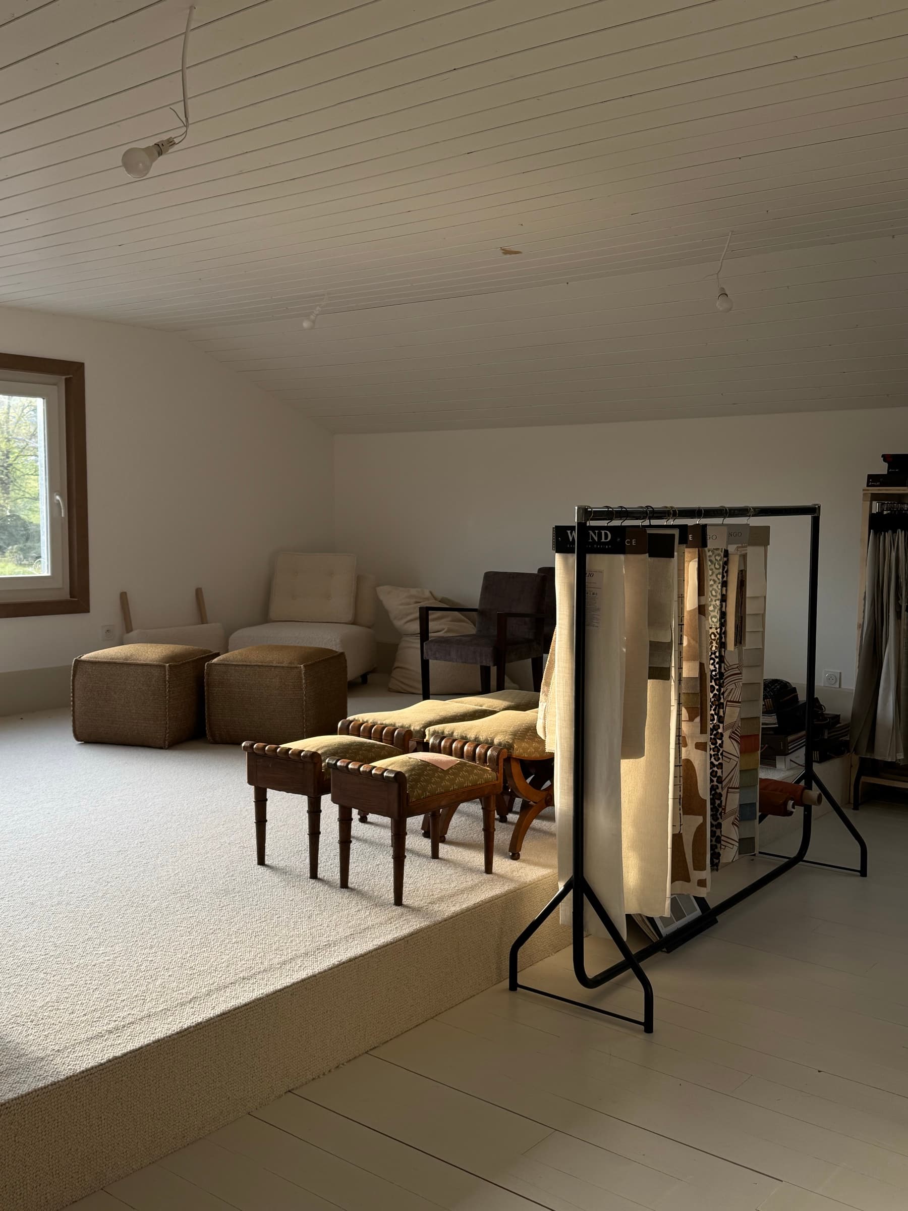 Sélection de tissus d'ameublement sur portant métallique, sièges et poufs tapissés dans le showroom de l'atelier